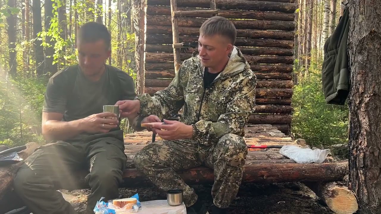 Two friends building a wooden house by hand — framing, saws, timber, and teamwork under a clear sky.